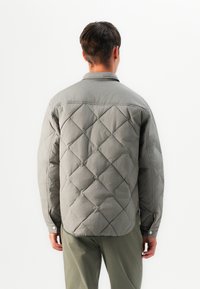 Quilted gray shirt jacket made of textured fabric, featuring a collared neck and buttoned cuffs, with a diamond pattern throughout.