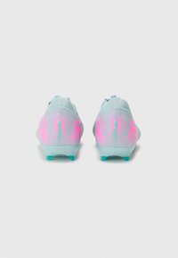 Des chaussures de football bleu clair avec des accents roses et bleus, présentant un design texturé et une silhouette basse pour améliorer la performance.