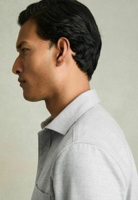 Grå skjorte med krave og tekstureret overflade, med en knaplukning og en enkelt brystlomme; vist på en model i profil.