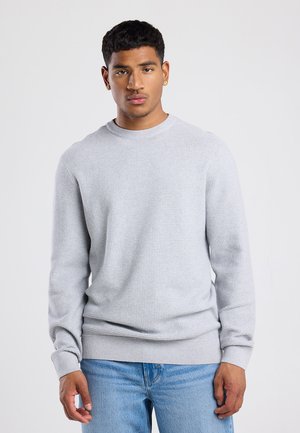Hellgrauer langärmeliger Pullover aus strukturiertem Stoff, Rundhalsausschnitt, gerippte Bündchen und Saum. Kombiniert mit blauen Jeans.