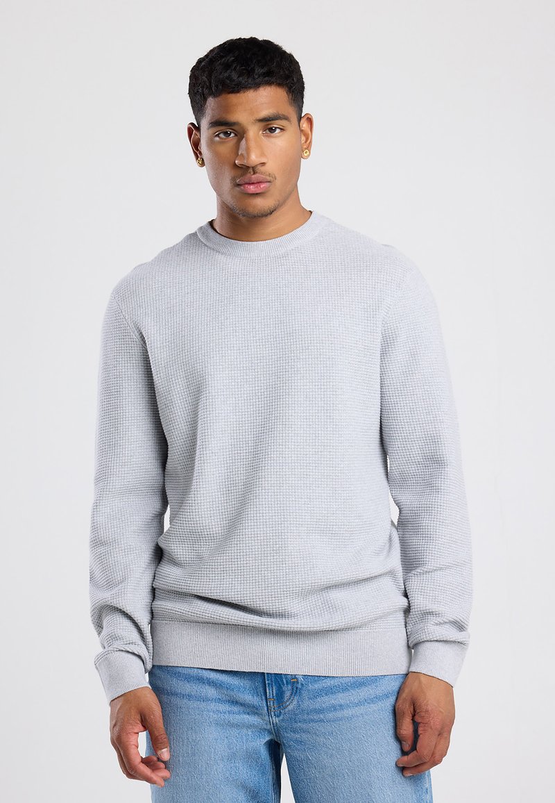 Light grey long-sleeve sweater with textured fabric, crew neckline, ribbed cuffs, and hem. Paired with blue jeans.