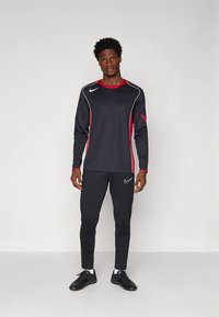 Black athletic outfit featuring a long-sleeve top with red accents and a white Nike logo, paired with black pants and black footwear.