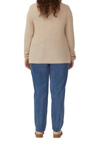 Beige gebreide trui met textuur en lange mouwen, gecombineerd met lichtblauwe spijkerbroek met een relaxte pasvorm en taps toelopende pijpen.