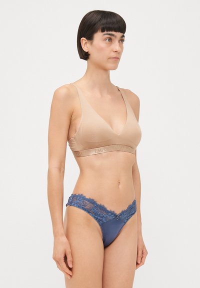 Beige draadloze bralette met een v-hals en een zachte textuur. Marineblauwe string versierd met kant langs de tailleband en benen.