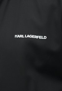 Μαύρο ύφασμα με λευκό λογότυπο "KARL LAGERFELD" τοποθετημένο στο κέντρο της επιφάνειας.