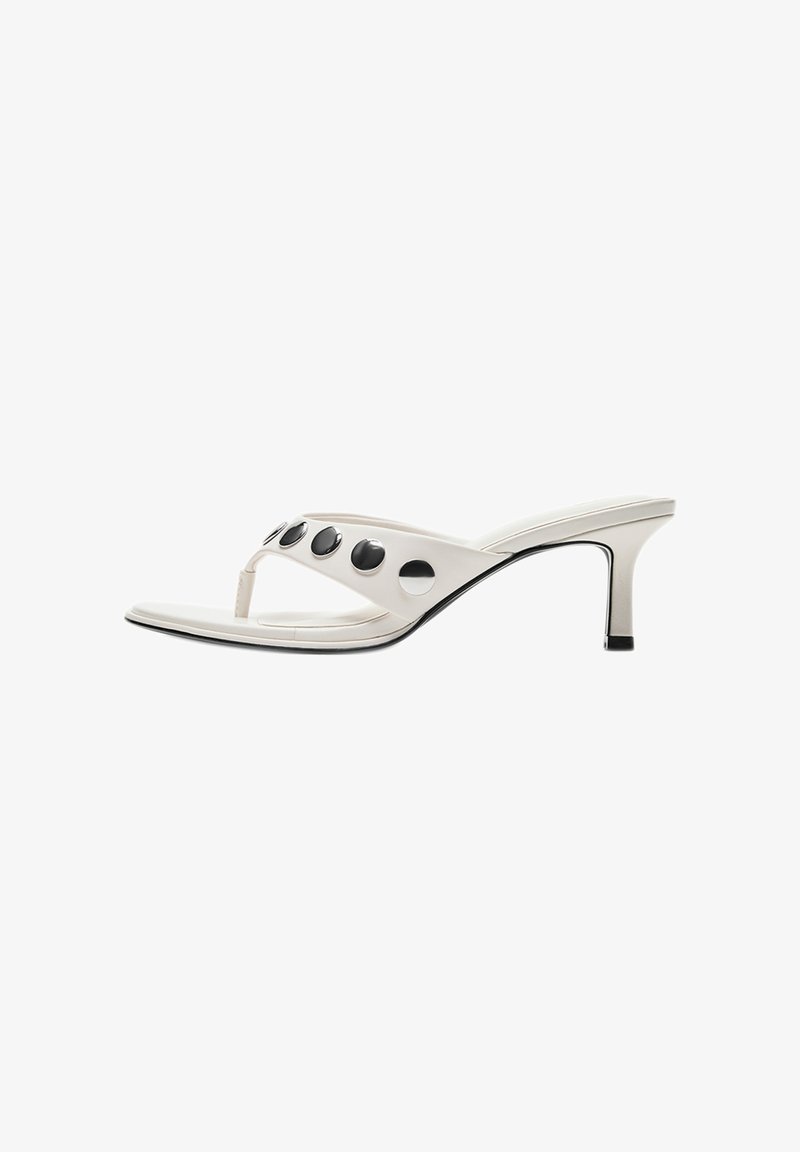 Sandale à talon blanche de style tongs avec un talon fin de hauteur moyenne et quatre gros clous ronds noirs sur la bride.