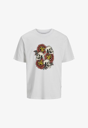 T-shirt en coton blanc présentant un graphique de crânes et de fleurs en rouge et noir. Associé à un jean bleu clair et des baskets beiges.