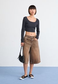 Black cropped long-sleeve shirt, tan wide-leg denim shorts, black handbag, and black slip-on shoes with white soles.