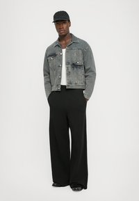 Jachetă din denim gri cu două buzunare frontale, cămașă albă și pantaloni negri largi. Completați cu o șapcă neagră și pantofi negri lucioși.