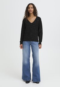 Black knit sweater with V-neck and silver speckles, paired with light blue wide-leg jeans. Both garments have a relaxed fit.