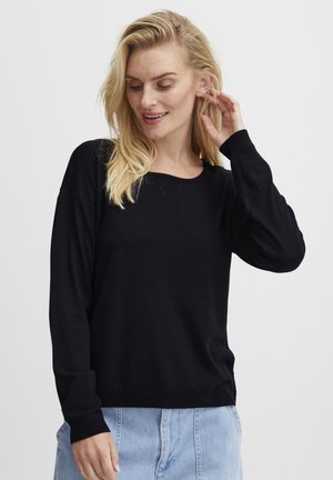 Pull en tricot noir avec un col rond, des manches longues et des poignets côtelés. Porté avec un short en denim bleu clair pour un look décontracté.