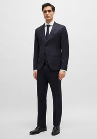 Jūrų laivyno kostiumas su įtemptu kirpimu, vieno mygtuko švarku, įpjautais atvartais ir dviem priekinėmis kišenėmis. Derinamas su balta marškiniais ir tamsia kaklaraiščiu. Juodi elegantiški batai.