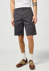 Pantaloni corti in denim grigio scuro con una vestibilità classica, caratterizzati da un taglio dritto, passanti per cintura e tasche frontali. Indossati con scarpe da ginnastica multicolori.