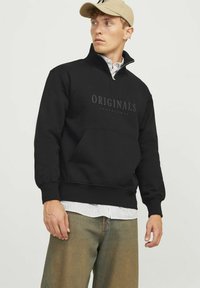 Schwarzer Kapuzenpullover mit hohem Kragen, ausgestattet mit einem Frontreißverschluss und einem großen "ORIGINALS"-Druck. Weiches Material, Kängurutasche und gerippte Bündchen.