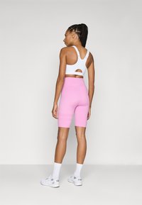 Sutien sport alb, ajustat, cu un design de spate decupat, asociat cu pantaloni scurți roz pentru bicicletă. Modelul poartă adidași albi și șosete de lungime medie.