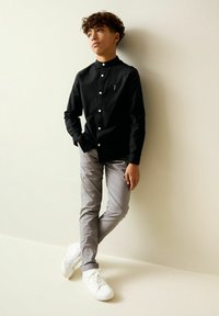 Camicia nera con bottoni e colletto alla coreana, pantaloni grigi aderenti e sneakers bianche. Design semplice con dettagli sottili sulla camicia.