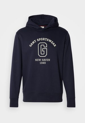 Marineblå hettegenser laget av bomull, med en frontlomme, ribbestrikkede ermer og et grafisk trykk med "GANT SPORTSWEAR" og "NEW HAVEN 1949."