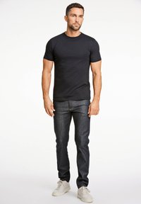 T-shirt nero a maniche corte abbinato a jeans in denim scuro e sneakers bianche. Il tessuto appare liscio; la vestibilità è aderente.