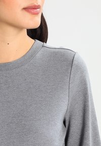 Harmaa neulotun collegepaita, jossa on pyöreä pääntie, pehmeä rakenne ja rento malli. Ominaisuuksiin kuuluu sileä, yksinkertainen muotoilu ilman kuvioita tai koristeita.