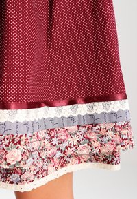 Jupe marron avec des pois blancs, bordée d'un ourlet floral rose et bleu, d'une bande rayée marine et d'une bordure en dentelle le long du bord inférieur.