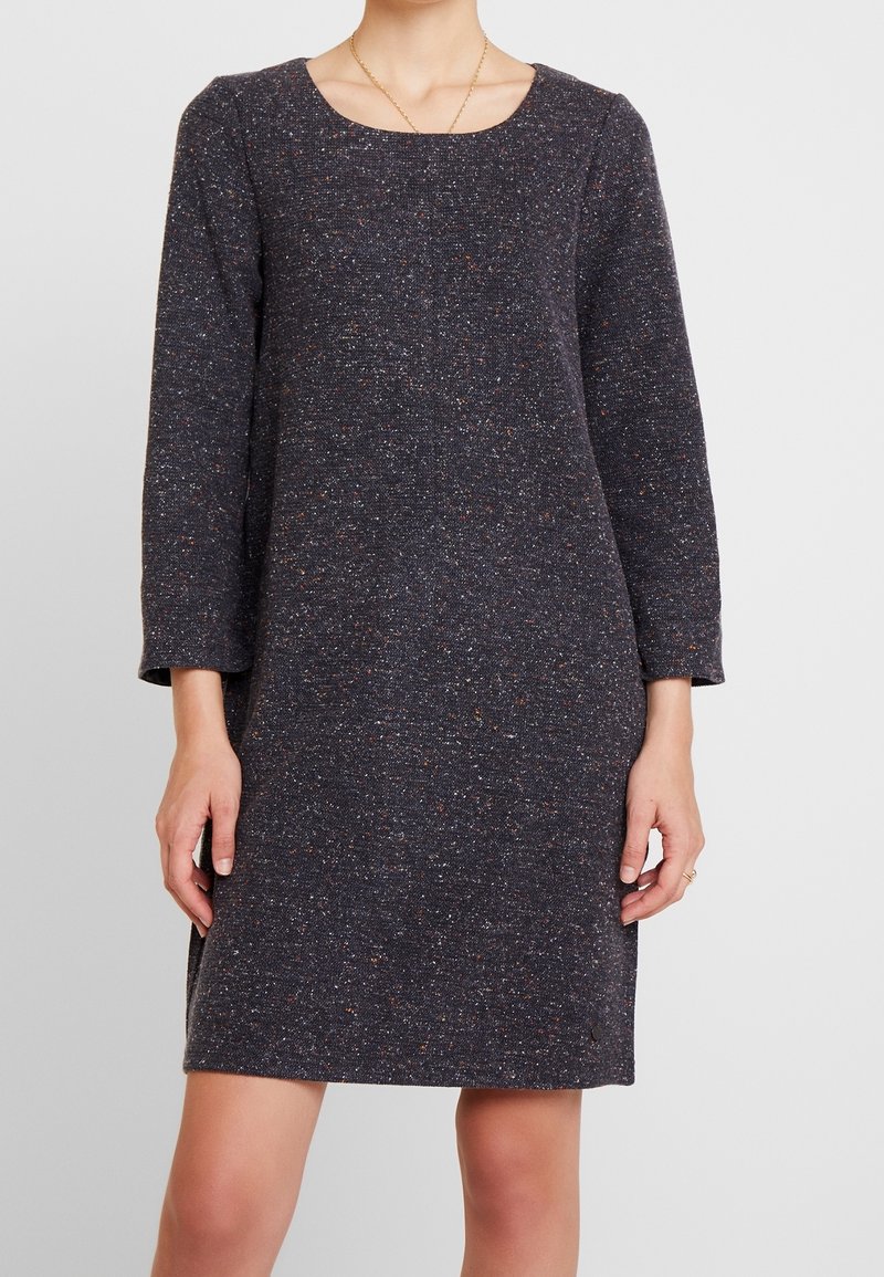 Robe gris foncé chinée avec un décolleté carré, manches longues et coupe droite. Le tissu présente de petites taches colorées pour la texture.