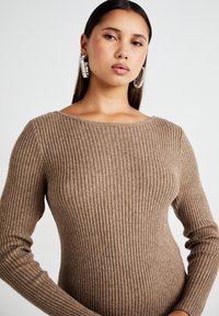 Pull en maille côtelée marron avec un col large et des manches longues, présentant une texture douce et une silhouette ajustée.