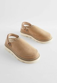 Tan suede slip-on shoes with backless design, soft lining, and light-colored rubber sole. Features contrasting stitching and decorative button accents.