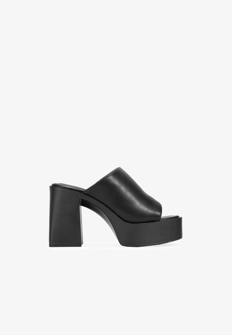Mules de plataforma de cuero negro con punta ancha y abierta, y un tacón grueso. Textura suave con un diseño minimalista y sin herrajes visibles.