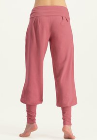 Rosa, verkürzte Hose mit breitem Bund, Falten an der Vorderseite und eng anliegenden Bündchen. Hergestellt aus weichem, dehnbarem Stoff.