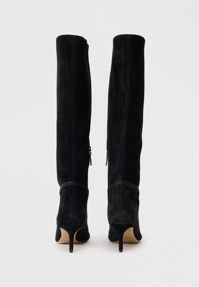 Υψηλές μαύρες σουέτ μπότες πάνω από το γόνατο με尖λή μύτη και λεπτό τακούνι. Διαθέτουν πλαϊνούς φερμουάρ και ορατές ραφές.