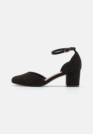 Schwarzer Wildleder-Schuh mit niedrigem Blockabsatz, geschlossener Spitze, offenen Seiten und einem Fersenriemen mit einer kleinen goldenen Schnalle.