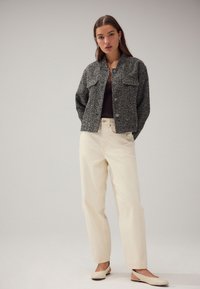 Czarna i biała teksturowana marynarka z tweedu z dwoma przednimi kieszeniami, zestawiona z kremowymi spodniami o prostych nogawkach oraz beżowymi wsuwanymi butami.