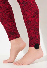 Leggings rossi con intricate fantaisie floreali e paisley neri, caratterizzati da un accent decorativo in pizzo nero alla caviglia. Tessuto morbido e elastico.
