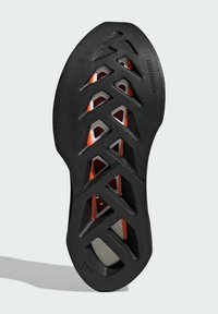 Black shoe sole with a textured surface, featuring a lattice design and orange accents beneath cut-out sections for lightweight flexibility.