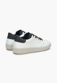 Witte leren sneakers met een zwarte hielkap, ronde neus en zwarte veters. Zachte textuur en een gevoerde, beige rubberen zool.