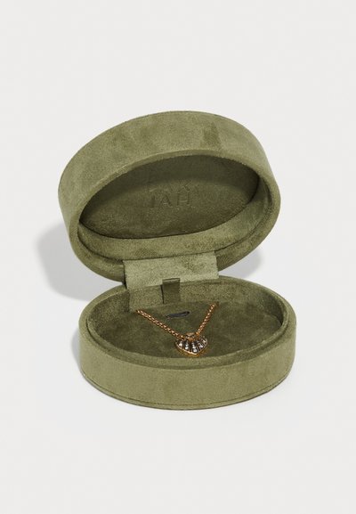 Caixa de joias em camurça verde com formato circular, contendo um colar em tom de ouro com um pendente em forma de concha com pedras transparentes.