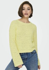Maglione giallo a textura con scollo rotondo e maniche lunghe a campana, abbinato a jeans in denim blu. Tessuto morbido e design dalla vestibilità ampia.