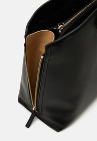 Sac à main en cuir noir avec une fermeture éclair dorée partiellement ouverte, montrant une doublure intérieure lisse couleur beige.