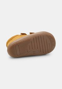 Chaussure en cuir marron avec une tige en daim doux, des bandes Velcro et une semelle en caoutchouc texturé présentant des motifs géométriques et la taille marquée "21."