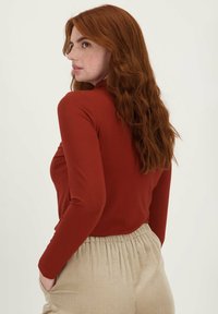 Langarmtop in roestbruin, getailleerd ontwerp, zachte textuur. Gecombineerd met beige, ribbelige hoge taille broek, met elastische tailleband en zakken.