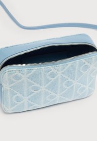 Μπλε τσάντα ώμου από καμβά με γεωμετρικό σχέδιο, ασημένιο φερμουάρ και δερμάτινες λεπτομέρειες. Το ανοιχτό πάνω μέρος αποκαλύπτει επενδυμένο εσωτερικό.