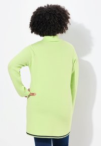 Tunic a maniche lunghe di colore verde chiaro in maglina con colletto alto e bordo nero all'orlo, caratterizzata da una vestibilità morbida e una superficie liscia.