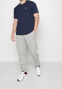 T-shirt a maniche corte blu navy, in cotone, pantaloni dal grigio, con polsini elasticizzati e sneakers bianche con accenti rossi. Logo Champion su entrambi gli articoli.