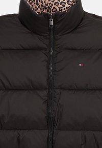 Sort puffervest med høj krave, lynlås og panelsyninger. Indersiden har et leopardprint-mønster. Lille logo i farve.