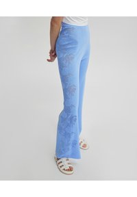 Lichtblauwe, uitlopende broek met textuur bloemenpatronen langs de zijkanten. Gemaakt van een geweven materiaal, met een hoge tailleband en een elastische pasvorm.