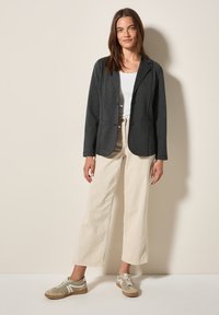 Blazer en tricot gris à deux boutons, porté sur un haut blanc. Associé à un pantalon large crème et des baskets grises avec des accents blancs.