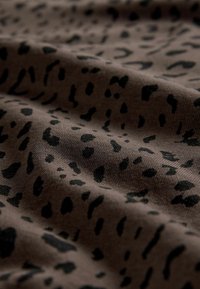 Hnedá tkanina s čiernym leopardím vzorom, zobrazujúca mäkkú textúru a jemné záhyby, ktoré zdôrazňujú pružnosť a dizajn materiálu.