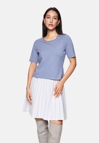 Helles blaues Kurzarmoberteil mit Rundhalsausschnitt; kombiniert mit einem weißen, gefalteten Rock mit silbernen Nadelstreifen; glatte Textur, lässige Passform.