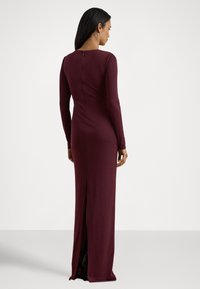 Dolga bordo obleka iz oprijete, gladke tkanine. Ima dolge rokave, zadrgo na hrbtu in stranski razporek za lažje gibanje.