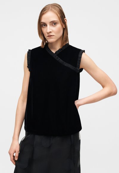 Svart sammetstopp med volangkrage och ärmar, utan ärmar. Slät textur och avslappnad passform med asymmetrisk halsringning.
